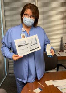 Wearing scrubs and a mask, nurse navigator, Lisa Schmidt, holds a stool-based colon cancer screening test.
