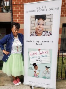 Dr. Liz posses with a sign promoting her book series "Little Lizzie"