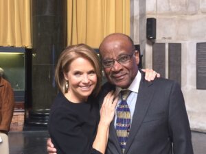 Katie Couric and Dr. Kenneth Forde in 2015, both are smiling at the camera. Couric's arm is on Forde's shoulder, and Forde's hand on her back. 