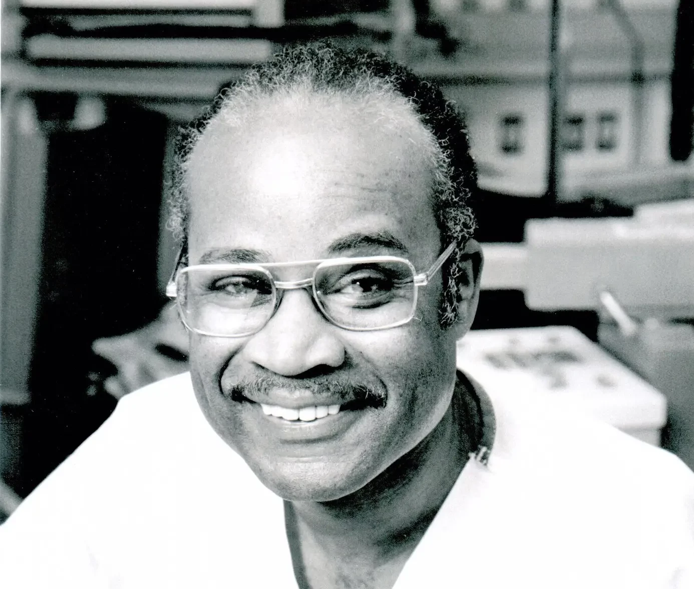 Dr. Kenneth Forde, the subject of the article in a black and white photo. Forde is smiling and wearing glasses. In the background is a surgical theater