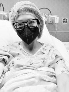 Black and white photo of Julie during treatment, wearing a mask and a hairnet