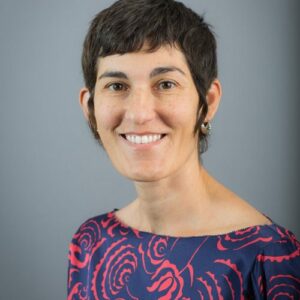 Dr. Lisa Soltani, Medical Director of Internal Medicine at El Rio health in Tucson, Arizona, smiles at the camera. She has dark brown hair, brown eyes. Her shirt has a flowery red pattern and a blue backdrop. 